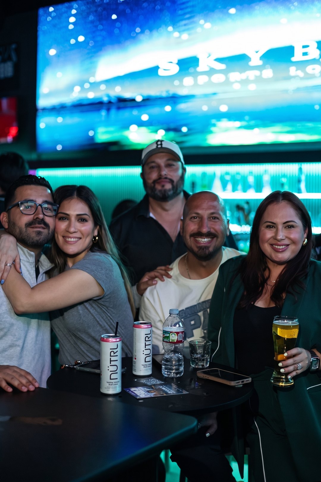 A group of friends at the SKYBOX bar, the SKYBOX aurora on the screen behind them