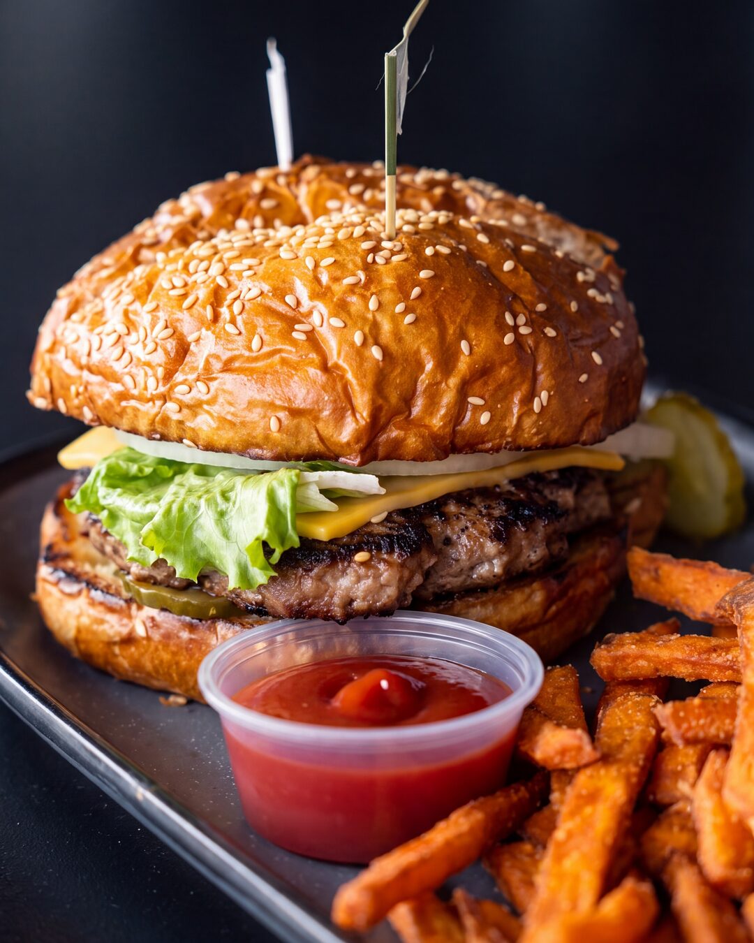 A cheeseburger with lettuce and pickles, served with sweet potato fries and ketchup